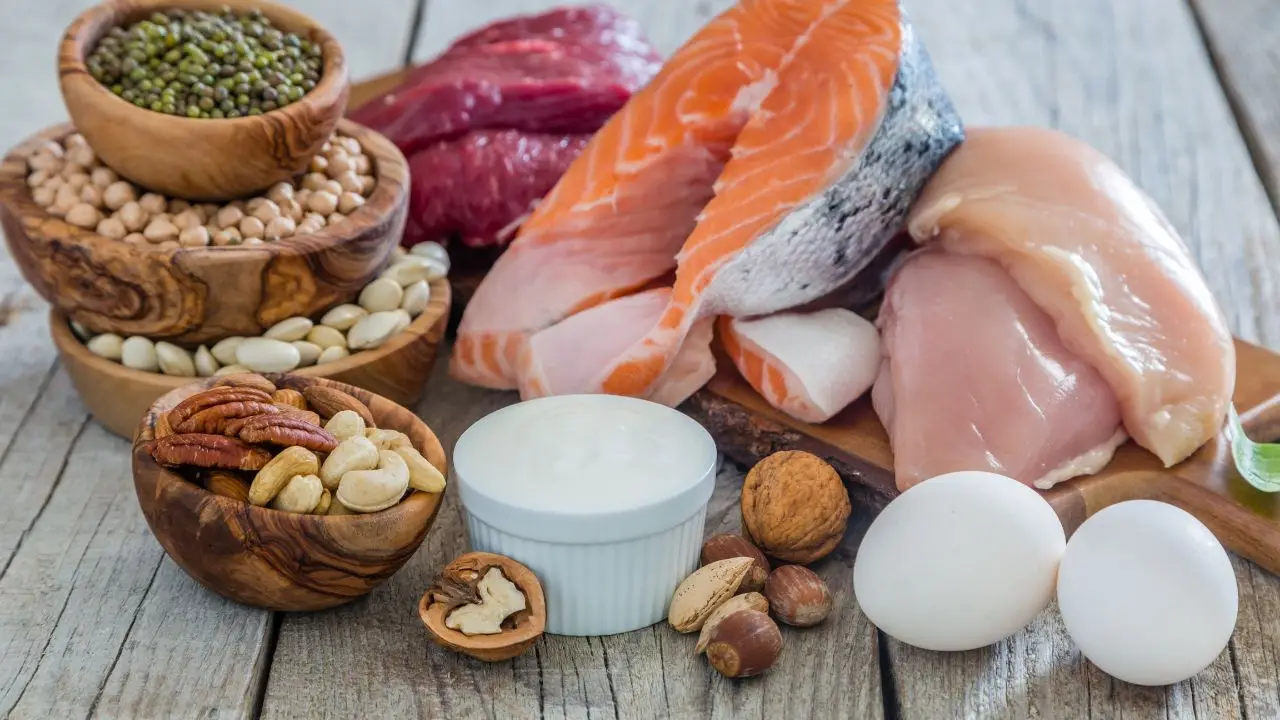 Healthy protein sources including salmon, chicken, assorted nuts, eggs, and legumes arranged on a wooden surface, emphasizing nutritious ingredients for a weight loss meal plan.
